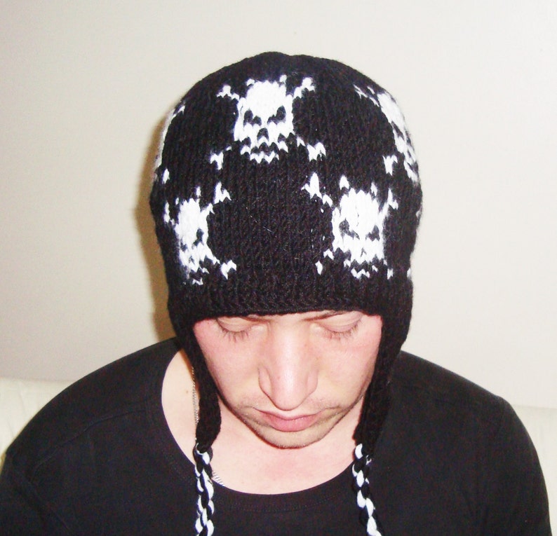 May include: Black knit beanie with white skull designs. The beanie has ear flaps and a long tassel.