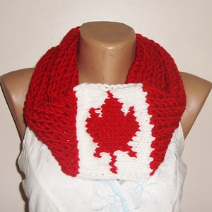 Puede incluir: Una bufanda de punto roja y blanca con un diseño de bandera canadiense. La bufanda está hecha de hilo suave y presenta una hoja de arce blanca sobre un fondo rojo.