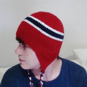 May include: Red knit hat with a white and blue striped band. The hat has ear flaps and a long cord.