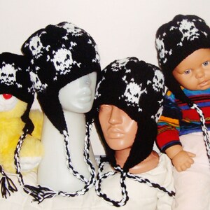 May include: Four black and white skull patterned knit hats with long ties. Two hats are on mannequins, one is on a teddy bear, and one is on a baby wearing a striped shirt.