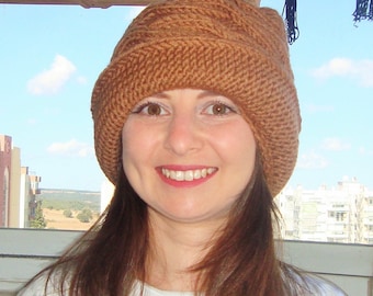 Puede incluir: Una mujer con el pelo largo y castaño lleva un gorro de punto marrón. Está sonriendo y mirando a la cámara.