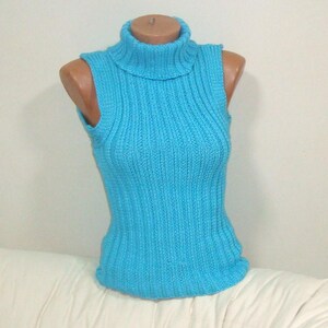 May include: A sleeveless, turquoise blue turtleneck sweater displayed on a mannequin. The sweater is made of a ribbed knit fabric. The turtleneck is folded over. The sweater is displayed on a mannequin.