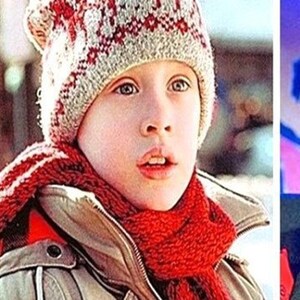 May include: A young person wearing a beige winter coat, a red scarf, and a knit hat with a red and white pattern. The person is looking up with a slightly open mouth. The image is a medium close-up.