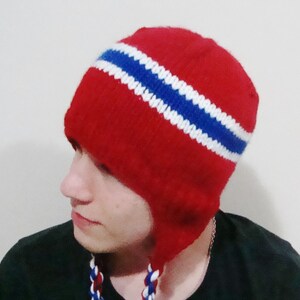 May include: Red knit hat with a white and blue stripe pattern. The hat has ear flaps and a pom pom on top.