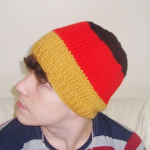 May include: A knitted beanie hat with black, red, and yellow stripes. The hat is worn by a person with brown hair.
