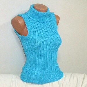 May include: A sleeveless, light blue knitted turtleneck top. The top is displayed on a mannequin and features a ribbed texture. The turtleneck is folded over. The top is made of a soft, possibly wool, material.