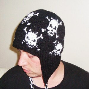 May include: Black knit beanie with white skull designs. The beanie has ear flaps and a long tassel.