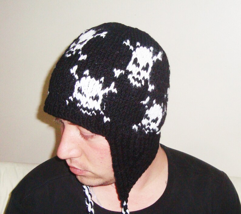 May include: Black knit beanie with white skull designs. The beanie has ear flaps and a long tassel.