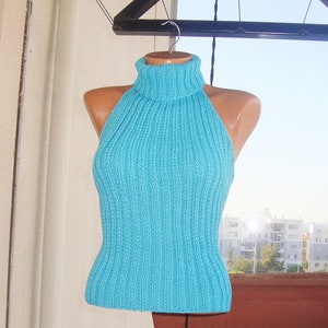 May include: A turquoise halter top with a ribbed knit design. The top features a high turtleneck and a fitted silhouette. The garment is displayed on a mannequin, showcasing its shape and texture. The background includes a view of a cityscape.