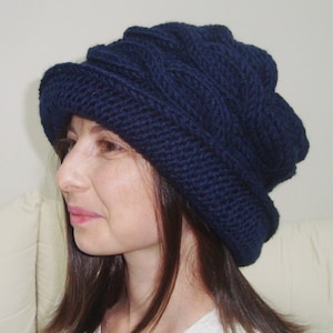 May include: A navy blue knitted hat with a slouchy, folded design. The hat is made of a soft, textured yarn and has a simple, classic style.