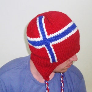 May include: A red knitted hat with a white and blue Norwegian flag design. The hat has a long, braided tassel.