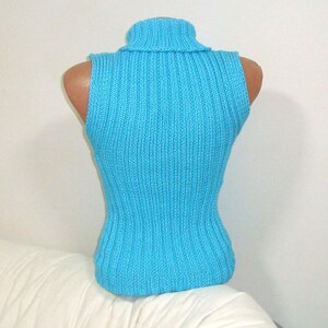 May include: A sleeveless, turquoise blue turtleneck sweater displayed on a mannequin. The sweater has a ribbed knit texture and a fitted silhouette. The turtleneck is folded over. The garment is displayed on a white background.