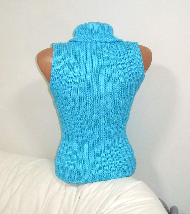 May include: A sleeveless, turquoise blue turtleneck sweater displayed on a mannequin. The sweater has a ribbed knit texture and a fitted silhouette. The turtleneck is folded over. The garment is displayed on a white background.