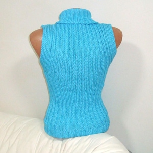 May include: A sleeveless, turquoise blue turtleneck sweater displayed on a mannequin. The sweater has a ribbed knit texture and a fitted silhouette. The turtleneck is folded over. The garment is displayed on a white background.
