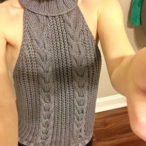 K&ouml;nnte beinhalten: Ein grauer Strickpullover mit Rollkragen und einem R&uuml;ckenausschnitt im Halterstil.