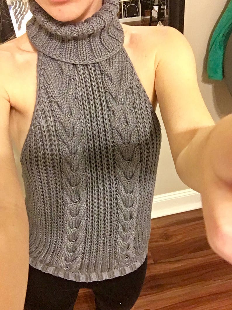 K&ouml;nnte beinhalten: Ein grauer Strickpullover mit Rollkragen und einem R&uuml;ckenausschnitt im Halterstil.