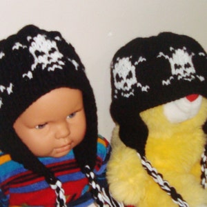 May include: Two black knit hats with white skull designs. The hats have long ties that can be tied under the chin. One hat is on a child's head and the other is on a yellow stuffed animal.