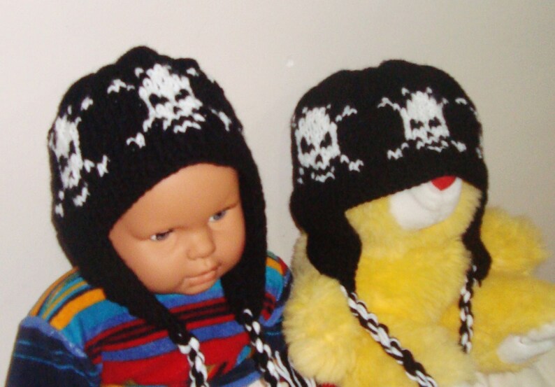 May include: Two black knit hats with white skull designs. The hats have long ties that can be tied under the chin. One hat is on a child's head and the other is on a yellow stuffed animal.