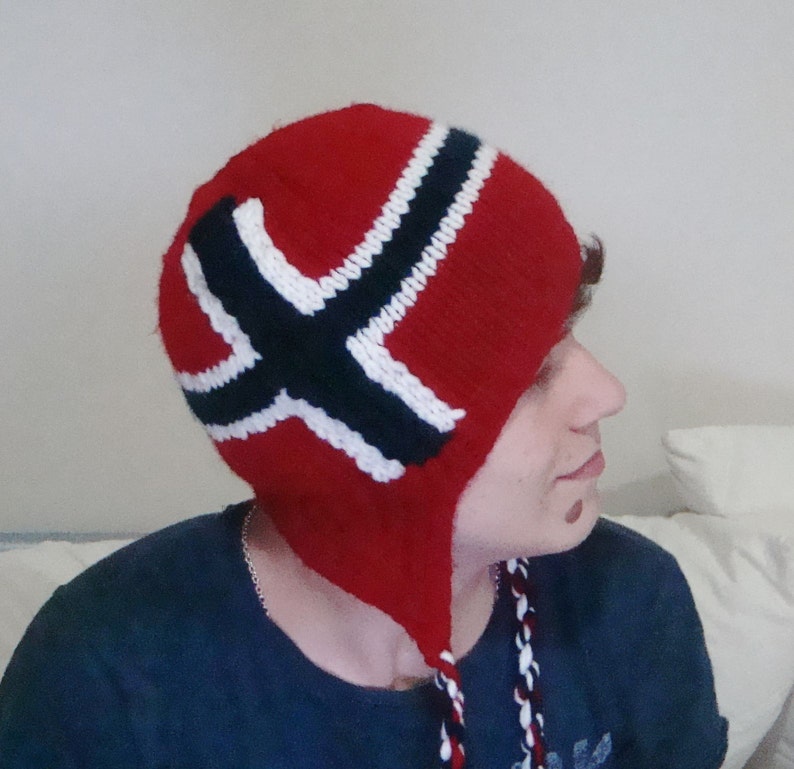 May include: A red knitted hat with a white and black Norwegian flag design. The hat has a long, pointed ear flap on each side.
