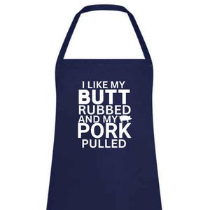 Może przedstawiać: Granatowy fartuch z białym napisem „I LIKE MY BUTT RUBBED AND MY PORK PULLED” i małą grafiką świni. Fartuch ma dekolt typu halter i dużą przednią kieszeń.