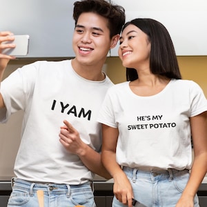 Op de afbeelding: Een stel draagt witte T-shirts met bijpassende tekst. Het shirt van de man zegt "IYAM" en het shirt van de vrouw zegt "He's my sweet potato". Ze lachen en maken een selfie.