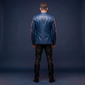 K&ouml;nnte beinhalten: Ein blauer Lederblazer und eine schwarze Lederhose. Der Blazer hat ein klassisches Design mit einem fallenden Revers und einem Zwei-Knopf-Verschluss. Die Hose ist eng anliegend und hat einen schlanken, modernen Look. Das Outfit ist vor einem dunkelblauen Hintergrund.