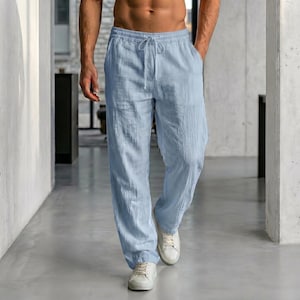 Puede incluir: Pantalones de lino azul claro con cintura con cordón y bolsillos. Los pantalones tienen un corte relajado y se combinan con zapatillas blancas. La tela parece ligera y adecuada para el clima cálido.