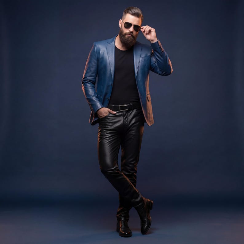 K&ouml;nnte beinhalten: Eine Person tr&auml;gt einen blauen Lederblazer, ein schwarzes T-Shirt, eine schwarze Lederhose und eine schwarze Sonnenbrille. Die Person steht mit einer Hand in der Tasche und der anderen an der Sonnenbrille. Der Hintergrund ist dunkelblau.