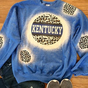 May include: Blue sweatshirt with a white bleach design of a basketball with the word "KENTUCKY" in white letters. The basketball has a leopard print pattern.