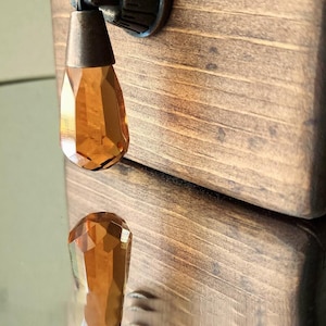 Peut inclure: Une bo&icirc;te en bois avec une finition brune et un bouton en cristal. Le bouton est de couleur ambre et a un design facett&eacute;. La bo&icirc;te est ferm&eacute;e.