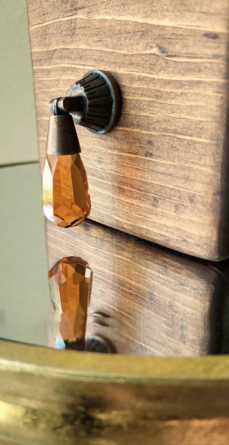 Peut inclure: Une bo&icirc;te en bois avec une finition brune et un bouton en cristal. Le bouton est de couleur ambre et a un design facett&eacute;. La bo&icirc;te est ferm&eacute;e.