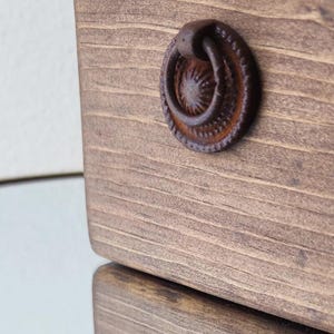 May include: Close-up of a rustic brown wooden drawer with a rusty metal ring pull handle.