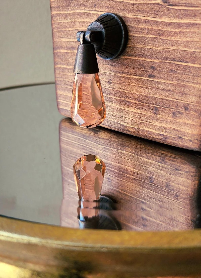 Peut inclure: Gros plan d'une bo&icirc;te en bois avec un bouton en cristal. Le bouton est en forme de larme et est de couleur p&ecirc;che clair. La bo&icirc;te est de couleur brun fonc&eacute; et pr&eacute;sente un motif de grain de bois.