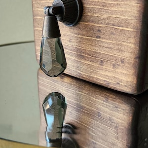 Peut inclure: Une bo&icirc;te en bois brun fonc&eacute; avec un bouton en m&eacute;tal noir et en verre transparent. Le bouton est en forme de larme et a un design facett&eacute;.