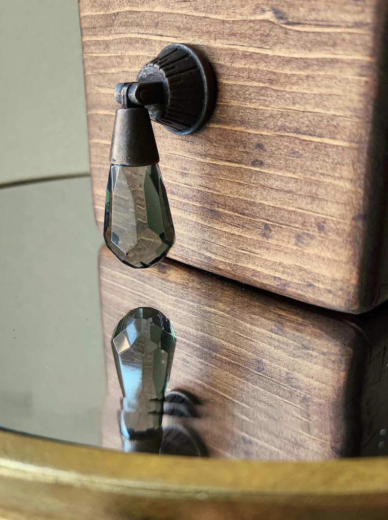 Peut inclure: Une bo&icirc;te en bois brun fonc&eacute; avec un bouton en m&eacute;tal noir et en verre transparent. Le bouton est en forme de larme et a un design facett&eacute;.