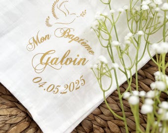 May include: White linen cloth with gold lettering that reads "Mon Baptême Galvin 04.05.2025". A white dove with an olive branch is above the text.