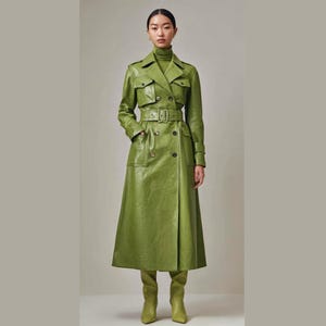 Könnte beinhalten: Ein langer, grüner Ledertrenchcoat mit doppelreihigem Design, Gürtel und passenden kniehohen Stiefeln. Der Mantel hat große Taschen und einen hohen Kragen. Das Model trägt einen grünen Rollkragenpullover.