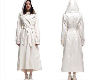 May include: A long, white hooded trench coat with a matching belt. The coat features a classic trench coat design with a double-breasted front, pockets, and a long, flowing skirt. The model is wearing white sneakers.