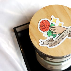 Könnte beinhalten: Ein Holzdeckel mit einem Aufkleber einer roten Rose, die von einer Hand gehalten wird, und einem Banner mit der Aufschrift "Ich bin eine gute Sache."
