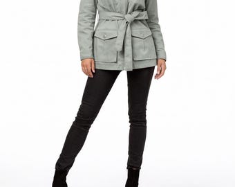 May include: A light green jacket with a tie belt, four front pockets, and a collared neckline. The jacket is paired with black pants and black ankle boots. The model is wearing a black and white striped turtleneck.