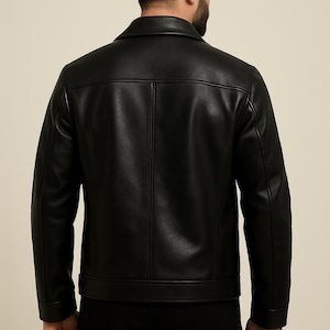 May include: Black leather jacket with a classic collar and a tailored fit. The jacket features a button closure and a clean, minimalist design. The back view showcases the jacket's structured silhouette and stitching details. A timeless outerwear piece.