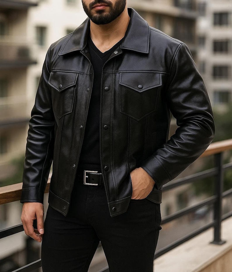 May include: Black leather jacket with a classic collar, two chest pockets, and button closures. The jacket is worn with a black shirt, black pants, and a black belt. The jacket has a tailored fit.