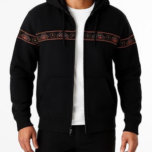 May include: Black zip-up hoodie with a hood and front pockets. The hoodie features a decorative band of orange and brown geometric patterns across the chest and sleeves. The model is wearing a white t-shirt underneath.