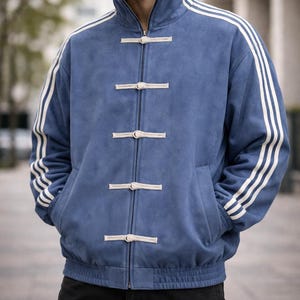 May include: A blue jacket with white stripes on the sleeves and a high collar. The jacket has a zipper closure and decorative toggles. The jacket has two front pockets and a ribbed hem.