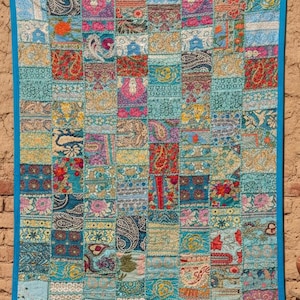 Può includere: Una trapunta patchwork con un vivace mix di colori e motivi. La trapunta presenta un bordo blu ed è composta da numerose toppe rettangolari in tonalità di verde acqua, rosa e arancione. Ogni toppa mostra intricati disegni floreali e paisley.