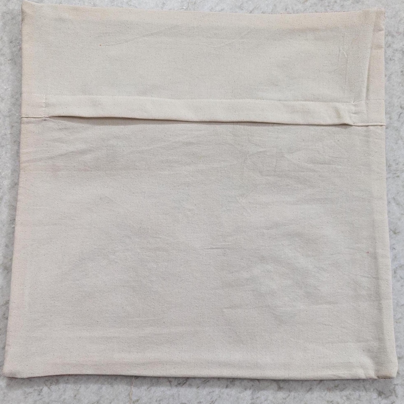 May include: A square, off-white pillow cover made of a textured fabric. The back of the pillow cover has a flap opening. The pillow cover is laying on a light gray surface.