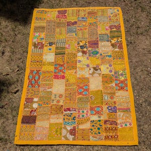 May include: A rectangular patchwork quilt with a yellow border. The quilt is composed of numerous fabric squares in shades of yellow, gold, orange, and brown. The squares feature various patterns and textures, creating a vibrant and textured textile.