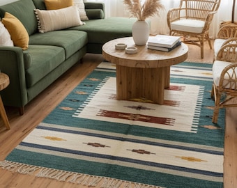 Puede incluir: Una alfombra de área de color verde azulado y crema con un patrón geométrico y flecos. La alfombra presenta un rectángulo central de color crema con un patrón repetido en marrón, amarillo y verde azulado. El borde tiene rayas verde azulado, crema y azul marino.