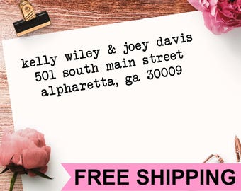 May include: A white rectangular card featuring black typewriter-style text that reads: kelly wiley & joey davis, 501 south main street, alpharetta, ga 30009. The card is secured with a black binder clip and decorated with pink flowers.