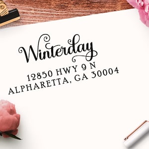 May include: A white card with black text that reads "Winterday" in a cursive font. Below the name is the address "12850 HWY 9 N ALPHARETTA, GA 30004".